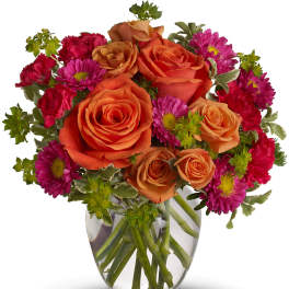 Bouquet of orange roses and magenta daisies in a clear glass vase