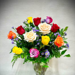 Mixed bouquet of multicolored roses and small purple flowers arranged in a clear glass vase