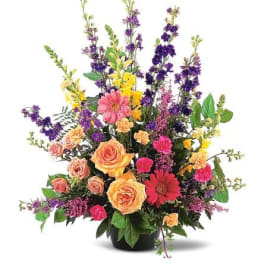 Tall mixed arrangement with orange roses, pink gerberas, carnations, and purple delphinium in a black container