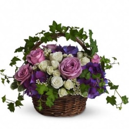 Lavender and white roses with purple blooms in a wicker basket with an ivy-covered handle.
