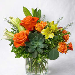 Orange roses and yellow blooms in a clear glass vase with a succulent centerpiece