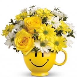 Yellow and white daisies with yellow roses arranged in a yellow smiley-face mug