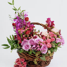 Basket arrangement of pink and purple roses with orchids and greenery