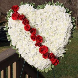 Heart-shaped standing wreath of white flowers with a diagonal line of red roses.
