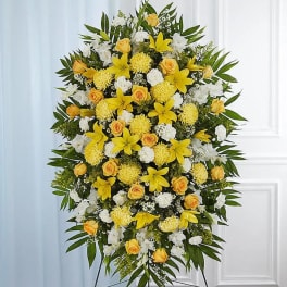 Tall yellow and white standing spray with lilies, roses, and carnations on a metal easel