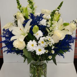 Tall vase arrangement of white lilies, roses, and daisies with bright blue filler flowers