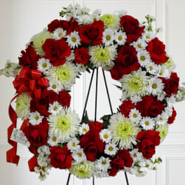 Standing wreath of red roses, white daisies, and green-tinted mums on a black easel with red ribbon bow