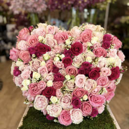 Heart-shaped arrangement of pink and white roses on a moss-covered base