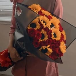 Person holding a bouquet of red roses and yellow flowers wrapped in black paper
