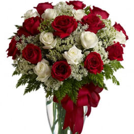 Red and white roses in a clear glass vase with a red ribbon