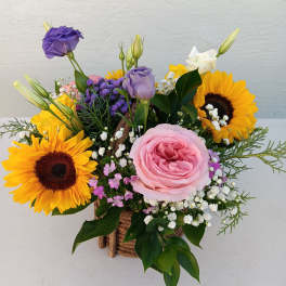 Mixed bouquet with sunflowers, pink rose, and purple lisianthus in a rustic basket