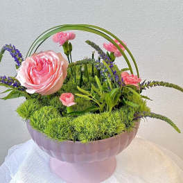 Pink roses and carnations arranged in a pink pedestal bowl