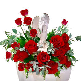 Red roses arranged around a white angel figurine in a vase.
