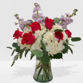 Arrangement of red roses, white hydrangeas, and light purple flowers in a clear glass vase