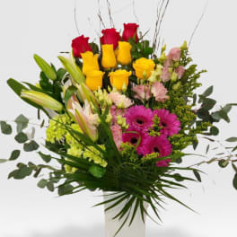Tall mixed bouquet of red and yellow roses, pink lilies and gerberas in a white vase