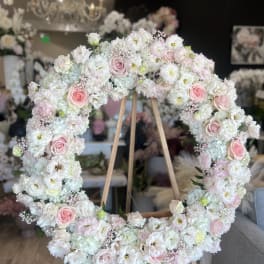 Large pastel floral wreath on a wooden easel with pink roses and white blooms