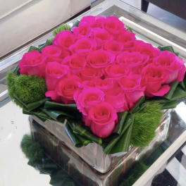 Hot pink roses arranged in a square glass box with green accents