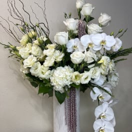 White roses and orchids arranged in a tall white vase