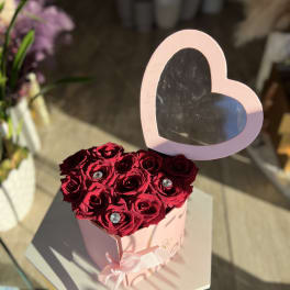 Heart-shaped box of red roses with a pink heart topper