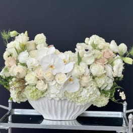 White floral arrangement in a white pedestal vase with pale blush roses and orchids