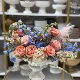 Bouquet of peach roses and blue flowers in a white pedestal vase