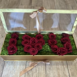 Open gold box with red roses arranged on green moss