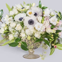 White floral arrangement in a glass compote vase with pink accents