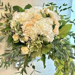 White hydrangeas and peach roses in a lush bouquet with greenery