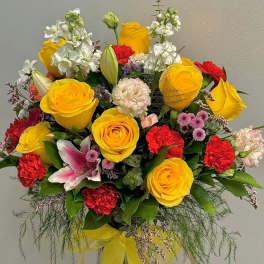 Bouquet of yellow roses, red carnations, and white flowers in a clear vase