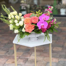 Mixed floral arrangement with roses, orchids, and pink blooms in a white pedestal vase