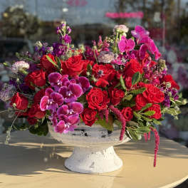 Red roses and pink orchids in a white pedestal bowl