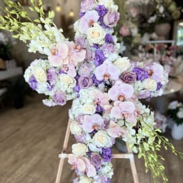 Cross-shaped floral arrangement with pink orchids, white roses, and purple blooms