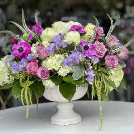 Pink and lavender flowers arranged in a white pedestal vase