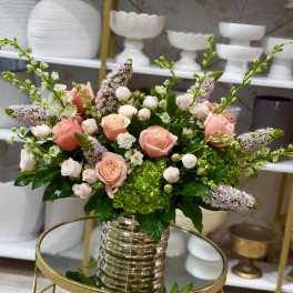 Peach and blush roses in a clear ribbed vase with green hydrangea and lilac spikes