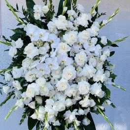 Large standing spray of white roses, orchids, and other white blooms on an easel.