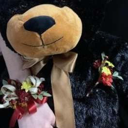 Teddy bear holding small floral accents and a ribbon