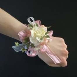 White rose wrist corsage with pink ribbon on a wrist