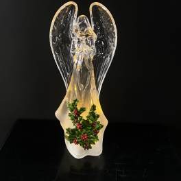 Glass angel figurine with holly decoration on a black background