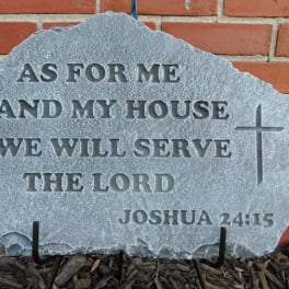 Engraved stone plaque with a Bible verse and cross against a brick wall