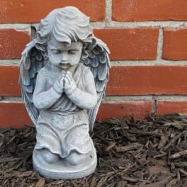 Stone angel statue kneeling in front of a brick wall