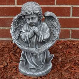 Gray angel statue with folded hands in front of a brick wall