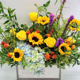 Bright mixed bouquet with sunflowers, yellow roses, and blue hydrangeas in a white box