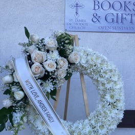 White floral funeral wreath on a wooden easel with a sympathy ribbon
