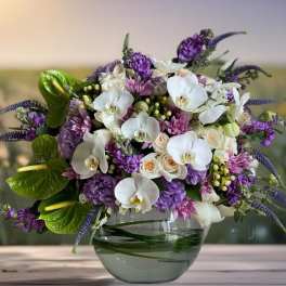 Purple and white floral arrangement in a glass bowl vase