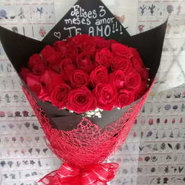 Bouquet of red roses wrapped in black paper with a pink ribbon