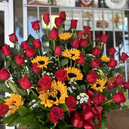 Basket arrangement of red roses and yellow sunflowers with a red ribbon