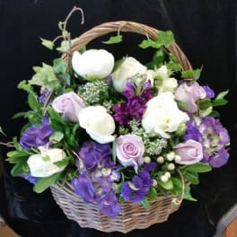 Basket arrangement of white and lavender roses with purple flowers