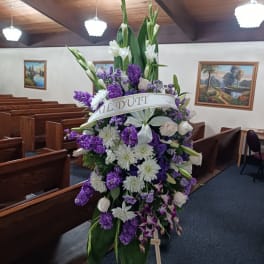 Tall funeral spray of white and purple flowers on an easel in a church