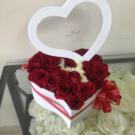 Heart-shaped box of red roses with a white heart topper and red ribbon