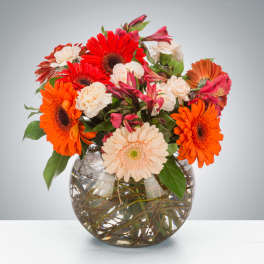 Mixed bouquet of orange, red, and cream flowers in a glass vase